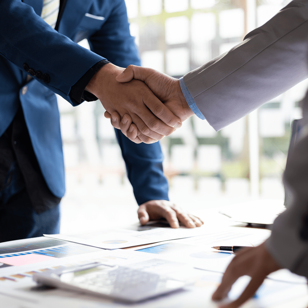 Two businesspeople shaking hands over documents in a meeting room.