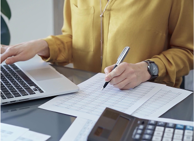 Person reviewing financial documents with a pen and laptop.