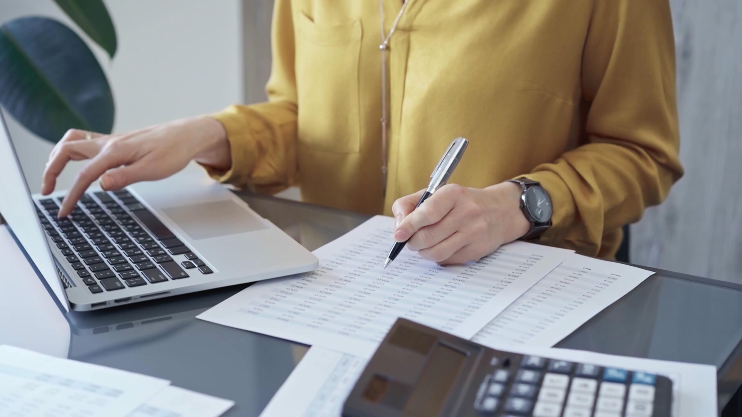 Person working on financial documents with a laptop and calculator.