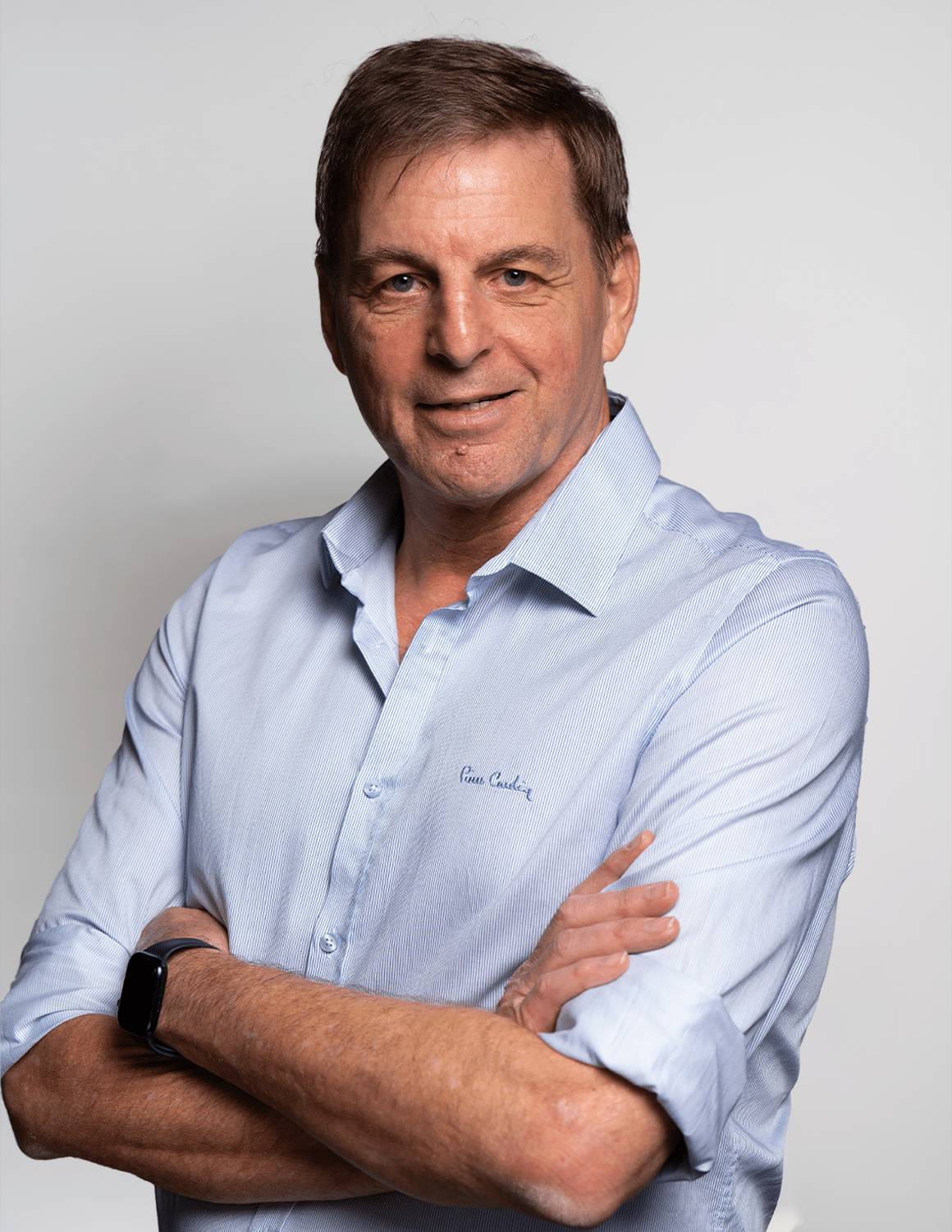 Confident man in a light blue shirt with arms crossed, smiling.